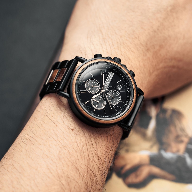 May include: A black wristwatch with a wooden bezel and band accents. The watch face is black with three sub-dials and the brand name "MONTIQUE". The watch is on a wrist.