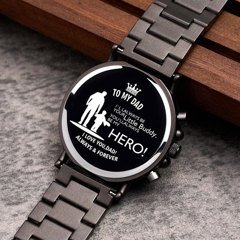 Puede incluir: Reloj de pulsera negro con una correa de metal gris oscuro. La esfera del reloj presenta el texto "TO MY DAD" y "HERO!" junto con una silueta de padre e hijo. El reloj tambi&eacute;n incluye las frases "I LOVE YOU, DAD! ALWAYS & FOREVER."