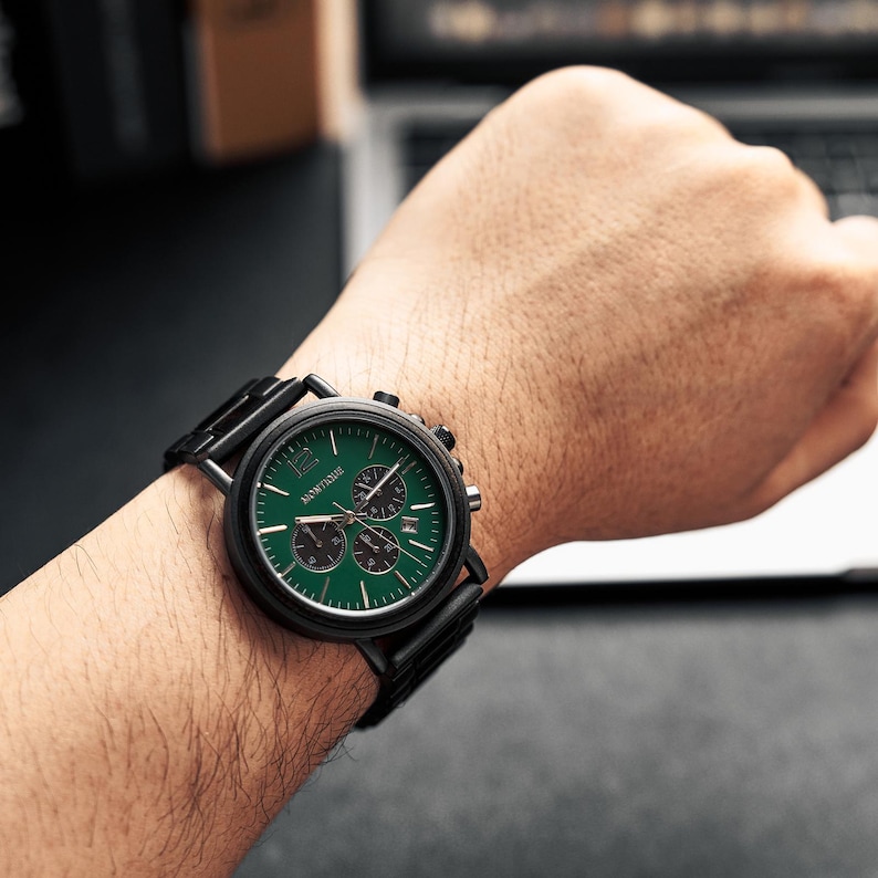 Puede incluir: Un reloj de pulsera negro con esfera verde y subesferas negras. El reloj tiene una correa de metal negro y se lleva en la mu&ntilde;eca. La esfera del reloj muestra el nombre de la marca y tiene marcadores de hora blancos.