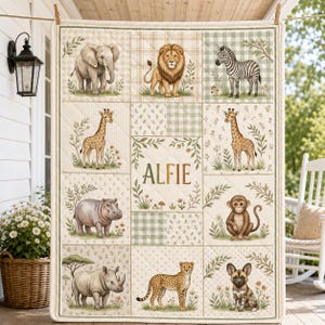 May include: A quilted baby blanket featuring a grid of illustrations of an elephant, lion, zebra, giraffe, hippo, monkey, rhino, cheetah, and wild dog. The center panel displays the name Alfie in brown text surrounded by botanical accents.