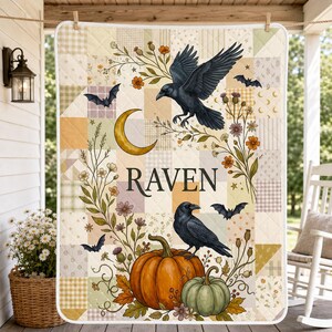 May include: A quilted throw blanket featuring a patchwork pattern in muted earth tones. The design includes two black ravens, a crescent moon, bats, pumpkins, and wildflowers. The word RAVEN is printed in the center in a black serif font.