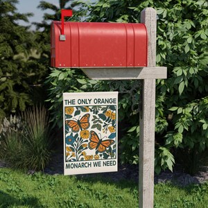 May include: A red mailbox with a flag up, mounted on a wooden post. A garden flag hangs below, featuring orange monarch butterflies, yellow flowers, and the text "THE ONLY ORANGE MONARCH WE NEED."