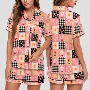 May include: A short-sleeve button-down pajama shirt and matching shorts set featuring a patchwork design. The pattern consists of alternating squares in pink, black and white gingham, and black floral prints with orange starburst accents.