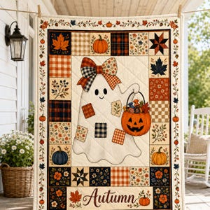 May include: A quilted throw blanket featuring a central white ghost character wearing a plaid bow and holding a jack-o'-lantern candy bucket. The border consists of patchwork squares with autumn-themed patterns, pumpkins, and the word Autumn.