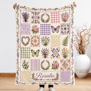 May include: A rectangular throw blanket featuring a patchwork grid design with floral, butterfly, and checkered patterns in shades of purple, pink, and green. The blanket includes the name Rosalie in script text and a lavender floral border.