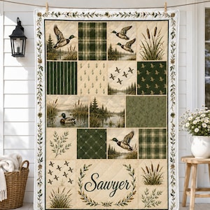 May include: A rectangular quilt featuring a patchwork design with various panels depicting mallard ducks in flight and on water, pine forests, cattails, and green plaid patterns. The bottom center panel displays the name Sawyer in script.