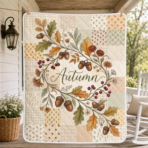 May include: A quilted blanket featuring a patchwork design of soft beige, cream, and sage green squares. The center displays a wreath of oak leaves, acorns, and red berries surrounding the word Autumn in a cursive script font.