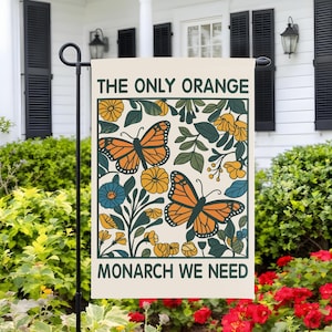 May include: A cream-colored garden flag with the text "THE ONLY ORANGE MONARCH WE NEED" in dark green. The flag features orange monarch butterflies, yellow and blue flowers, and green leaves.