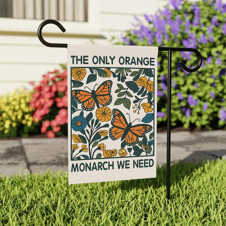 May include: A rectangular garden flag with the text "THE ONLY ORANGE MONARCH WE NEED" and a design featuring orange monarch butterflies, yellow flowers, and green leaves. The flag is displayed on a black metal stand in a garden setting.