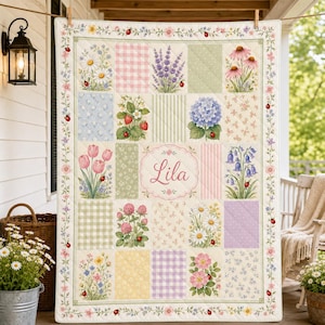 May include: A quilted blanket featuring a grid of floral and patterned squares, including daisies, lavender, strawberries, hydrangeas, tulips, and clover. The center square displays the name Lila in cursive script, surrounded by a ladybug border.