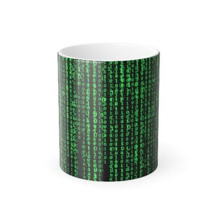 May include: A white ceramic mug with a black and green design featuring a repeating pattern of binary code. The code is green and appears to be flowing down the mug.