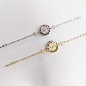 May include: Two wristwatches with octagonal cases and thin metal link bracelets. One watch is silver-toned with a white face, and the other is gold-toned with a matching gold face. Both feature small flower-shaped accents on the bracelet links.