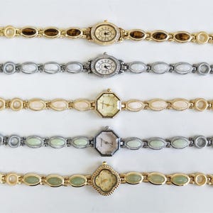 May include: Five wristwatches arranged horizontally. The top watch has a gold-tone band with brown oval inlays and a round face. The second is silver-tone with white oval inlays. The third is gold-tone with cream inlays and an octagonal face. The fourth is silver-tone with pale green inlays and an octagonal face. The bottom watch is gold-tone with light green inlays and a clover-shaped face.