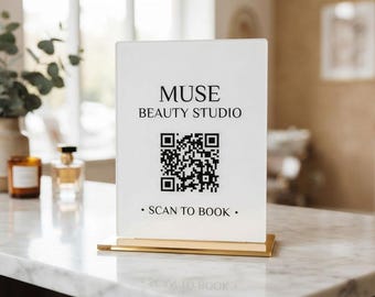 May include: A rectangular white acrylic sign with a gold metal base featuring the black text MUSE BEAUTY STUDIO, a central QR code, and the text SCAN TO BOOK at the bottom. The sign is designed for display on a flat surface for business use.