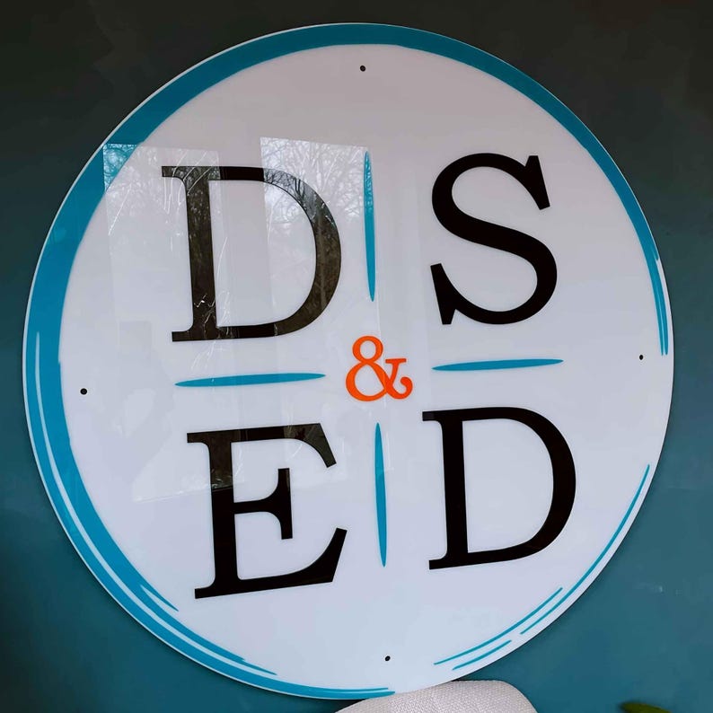 May include: A white circular sign with a blue border and the text "D & S ED" in black letters. The ampersand is in orange.