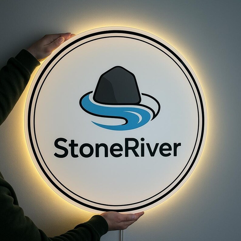 Peut inclure: Un panneau rond et lumineux avec le texte "StoneRiver" en noir. Le panneau pr&eacute;sente un logo d'un rocher gris au-dessus d'une rivi&egrave;re bleue. Le panneau est tenu par des mains et a une face blanche avec une bordure noire et une lueur jaune chaude.