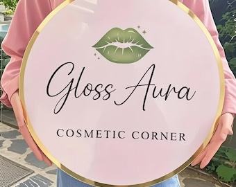 Puede incluir: Un letrero redondo con fondo rosa y borde dorado. El letrero presenta el texto "Gloss Aura" en escritura negra, un gráfico de labios verdes y las palabras "Cosmetic Corner" en mayúsculas negras.