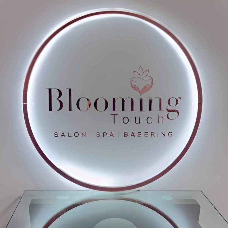 May include: A circular sign with the words "Blooming Touch" in a stylized font. The sign has a glowing white interior and a rose gold border. Below the main text are the words "Salon | Spa | Babering".