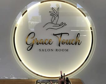 Puede incluir: Letrero circular de salón con el texto "Grace Touch SALON ROOM" en dorado y negro. El letrero tiene un borde dorado y un diseño de mano. Una bandeja con herramientas y productos para el cuidado de las uñas se encuentra debajo.