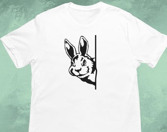 May include: White t-shirt with a black graphic of a rabbit peeking around a corner.