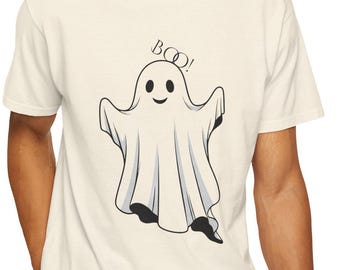 May include: Cream-colored t-shirt featuring a cartoon ghost with the word "BOO!" above it. The ghost has a friendly expression and is outlined in black. The shirt is a casual, everyday wear item.