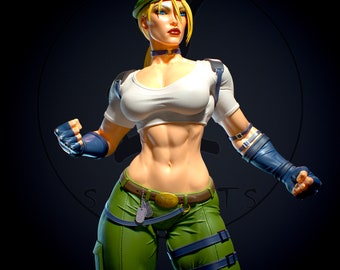 May include: A female action figure with blonde hair, wearing a green military-style outfit, a white tank top, and a green beret. She has a determined expression and is holding her fists up.