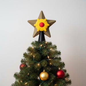 Peut inclure: Un sommet de sapin de Noël en forme d'étoile. L'étoile est de couleur or mat avec un centre jaune et rouge. L'arbre est décoré de lumières et de boules.