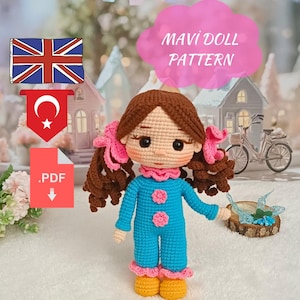 May include: A handmade crochet doll with brown hair styled in pigtails, wearing a blue jumpsuit with pink accents. The doll has a pink ruffled collar and yellow shoes. The image includes the text "MAVI DOLL PATTERN" and a PDF download icon.