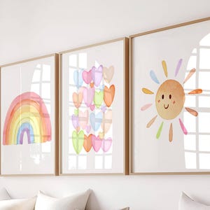 May include: Three framed watercolour prints featuring a rainbow, a cluster of colourful hearts, and a smiling sun with rainbow rays.