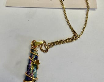 May include: A gold-colored chain necklace with a pendant. The pendant is a colorful, iridescent stone wrapped in gold wire, with a small gold star accent. The card behind the necklace reads "Lilly and the Treasure".