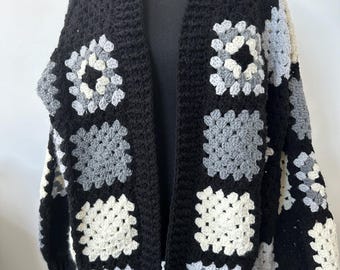 Puede incluir: Chaqueta de punto de ganchillo negra con un patrón de cuadrados de la abuela en tonos grises y blancos.