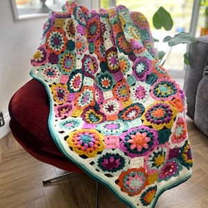 Può includere: Una colorata coperta all'uncinetto fatta a mano drappeggiata su una sedia rossa. La coperta presenta un motivo floreale nei toni del rosa, arancione, giallo, verde e bianco, con un bordo turchese. La coperta misura circa 152 cm di larghezza e 178 cm di lunghezza.
