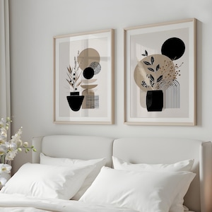 Può includere: Due stampe artistiche astratte incorniciate. Ogni stampa presenta un vaso nero con elementi botanici, forme geometriche e tonalità neutre. L'opera d'arte è esposta sopra un letto con biancheria da letto bianca, creando un'estetica moderna e minimalista.