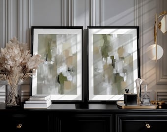 May include: Two framed abstract art prints with black frames. The artwork features a blend of green, beige, white, and gray brushstrokes. The prints are displayed on a black cabinet, alongside decorative items like a vase and books.