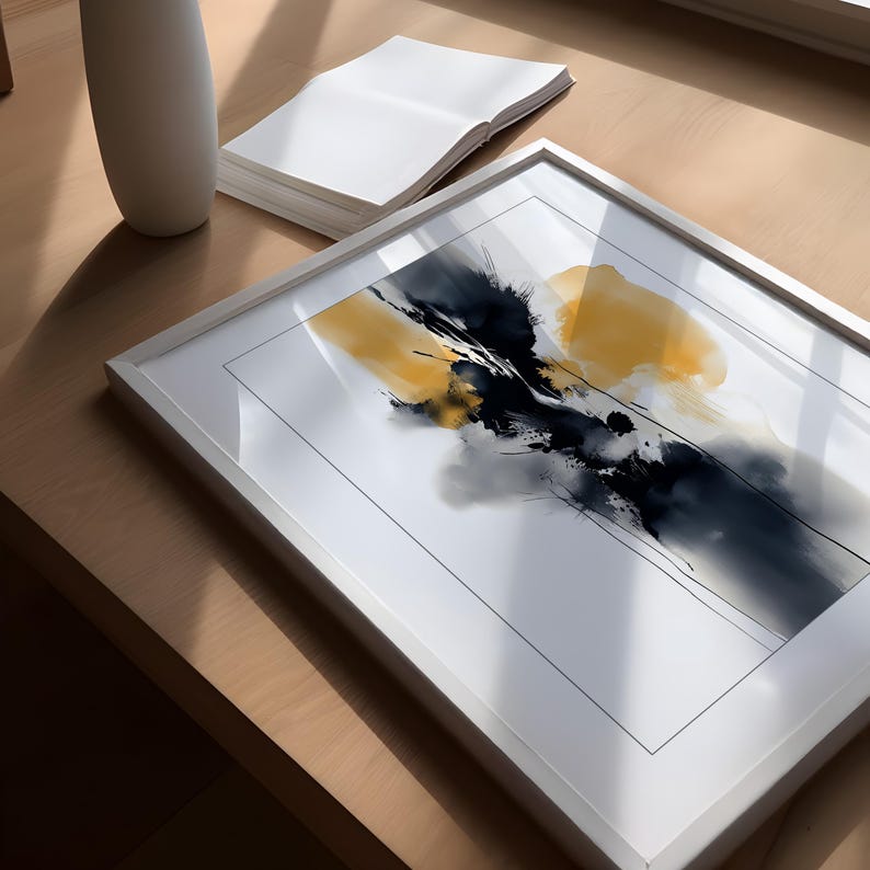 May include: White framed abstract art print with a watercolour design of black, yellow, and grey brushstrokes. The artwork is on a wooden surface, with a white vase and a stack of white paper.