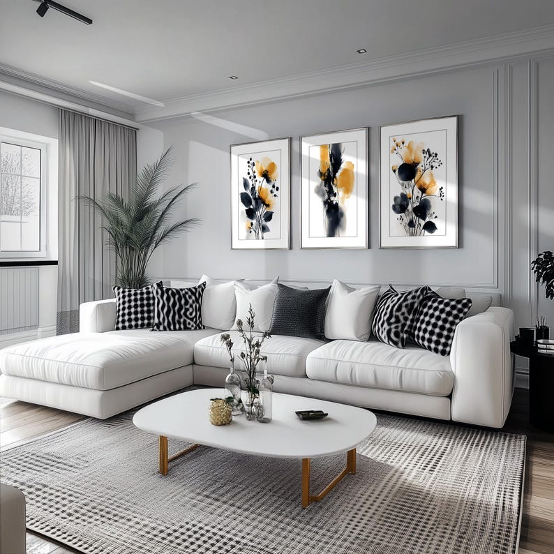 May include: A contemporary living room with a white corner sofa and cushions in monochrome patterns. Three framed abstract floral prints adorn the wall. A white oval coffee table with gold legs rests on a patterned rug.