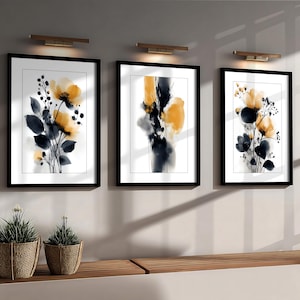 May include: Three framed floral art prints. Each print features a watercolour design with yellow and black flowers and dark blue leaves against a white background. The frames are black, and the art is displayed on a light grey wall.