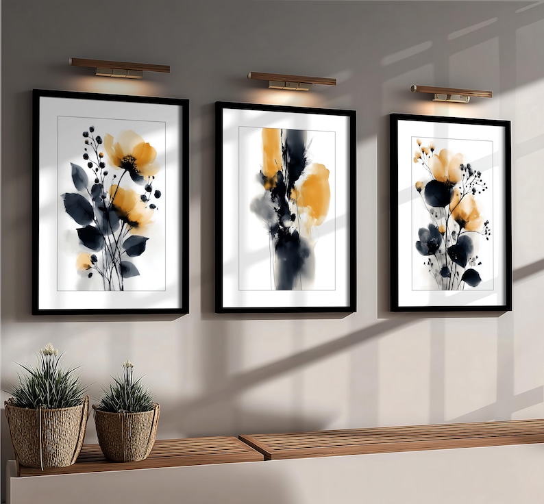 May include: Three framed floral art prints. Each print features a watercolour design with yellow and black flowers and dark blue leaves against a white background. The frames are black, and the art is displayed on a light grey wall.