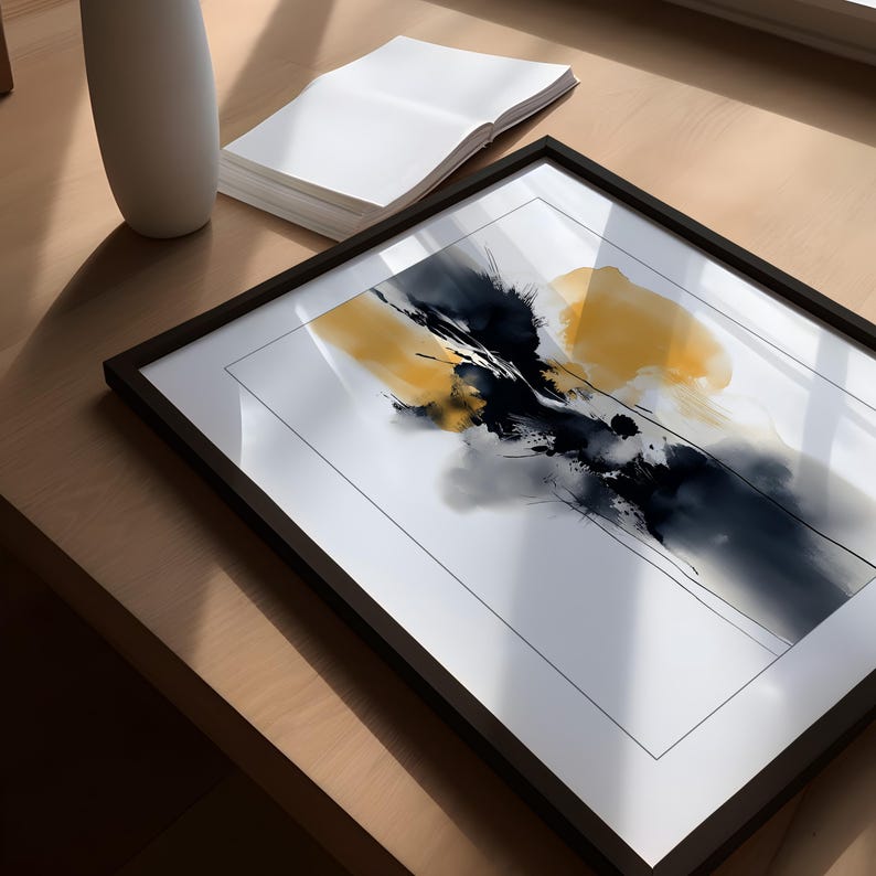 May include: Abstract art print in a black frame. The artwork features a dynamic composition of yellow, black, and grey brushstrokes on a white background. A white vase and a stack of white papers are also visible.