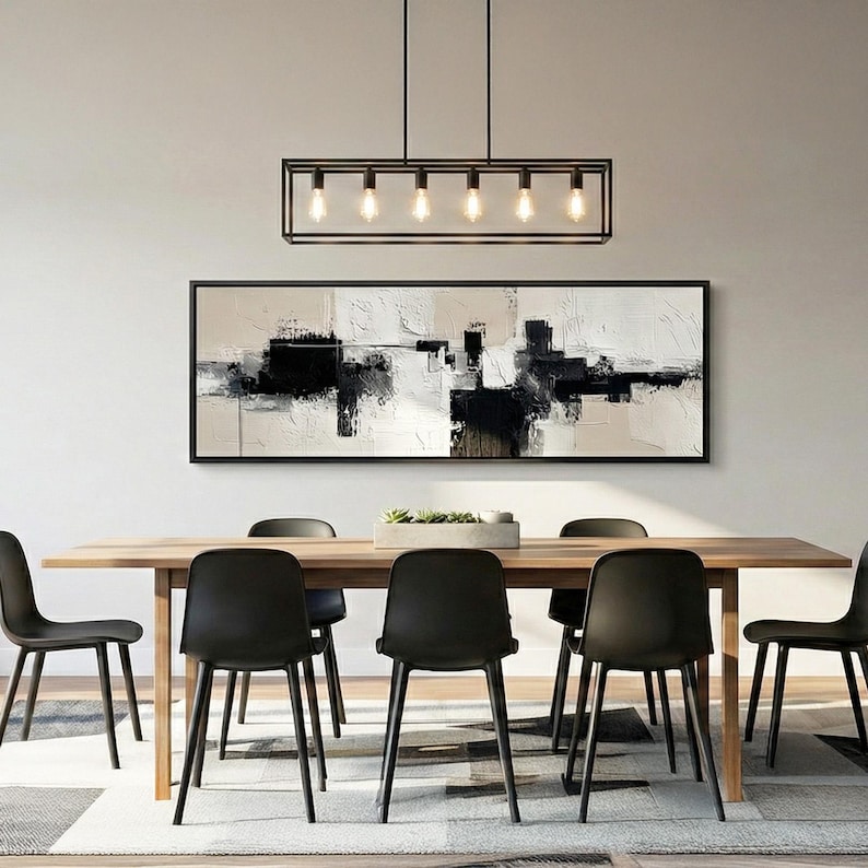 May include: A modern dining room set featuring a rectangular wooden table with six black chairs. Above the table hangs a rectangular black light fixture with six bulbs. A large abstract black and white painting hangs on the wall.