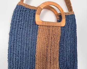 Puede incluir: Un bolso tote tejido con un diseño de bloques de color azul y marrón. El bolso tiene un asa de madera y una correa de hombro tejida. El bolso está hecho de un material texturizado y es adecuado para llevar varios artículos.