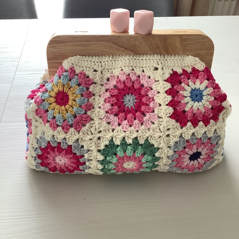 Puede incluir: Un bolso de crochet con marco de madera y estampado floral de colores. El bolso est&aacute; hecho con cuadrados de granny en tonos de rosa, azul, verde y blanco.