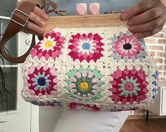 May include: A white crocheted bag with a wooden frame and pink, blue, and green floral designs. The bag has a brown leather strap.