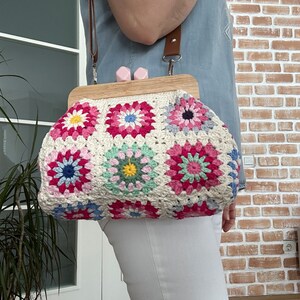 Puede incluir: Un bolso de crochet con un marco de madera y una correa marr&oacute;n. El bolso est&aacute; hecho de cuadrados coloridos con un patr&oacute;n floral.