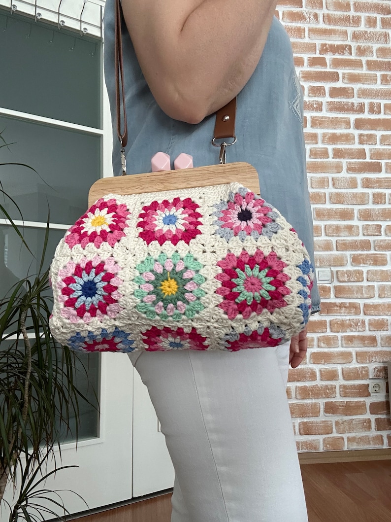 Puede incluir: Un bolso de crochet con un marco de madera y una correa marr&oacute;n. El bolso est&aacute; hecho de cuadrados coloridos con un patr&oacute;n floral.