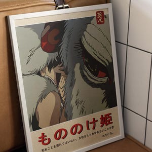 May include: A vintage-style poster featuring a character from the animated film Princess Mononoke. The poster is in a white frame and has a red Japanese character in the top right corner. The text on the poster reads "もののけ姫" and "死ぬことを恐れてはいない。大切な人々を守れないことを恐れている。"
