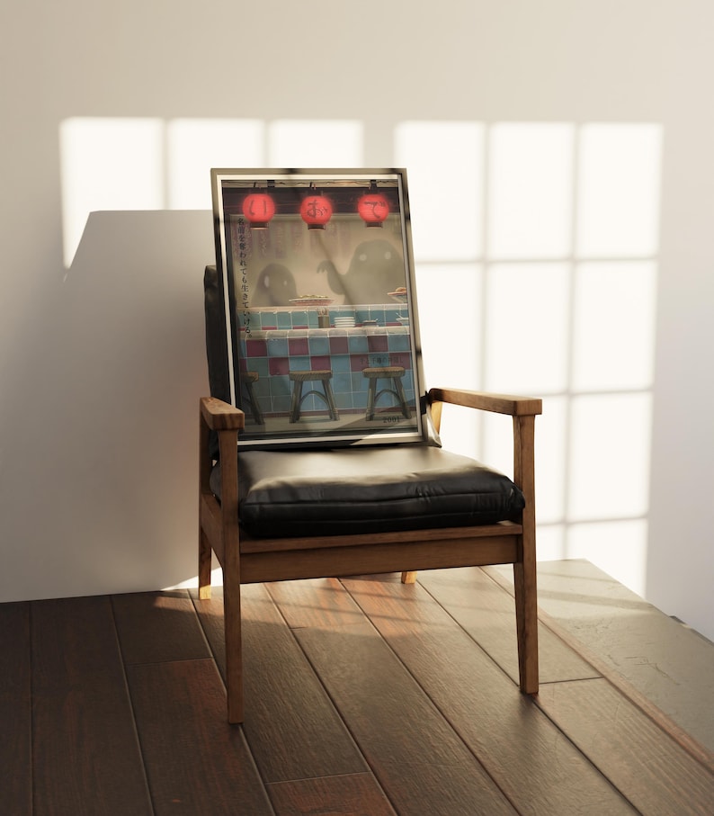 Puede incluir: Una impresi&oacute;n enmarcada que representa una escena de restaurante japon&eacute;s con linternas rojas, figuras fantasmales y taburetes. La impresi&oacute;n est&aacute; apoyada en una silla de madera con asiento de cuero negro. El fondo es una pared blanca con luz solar.