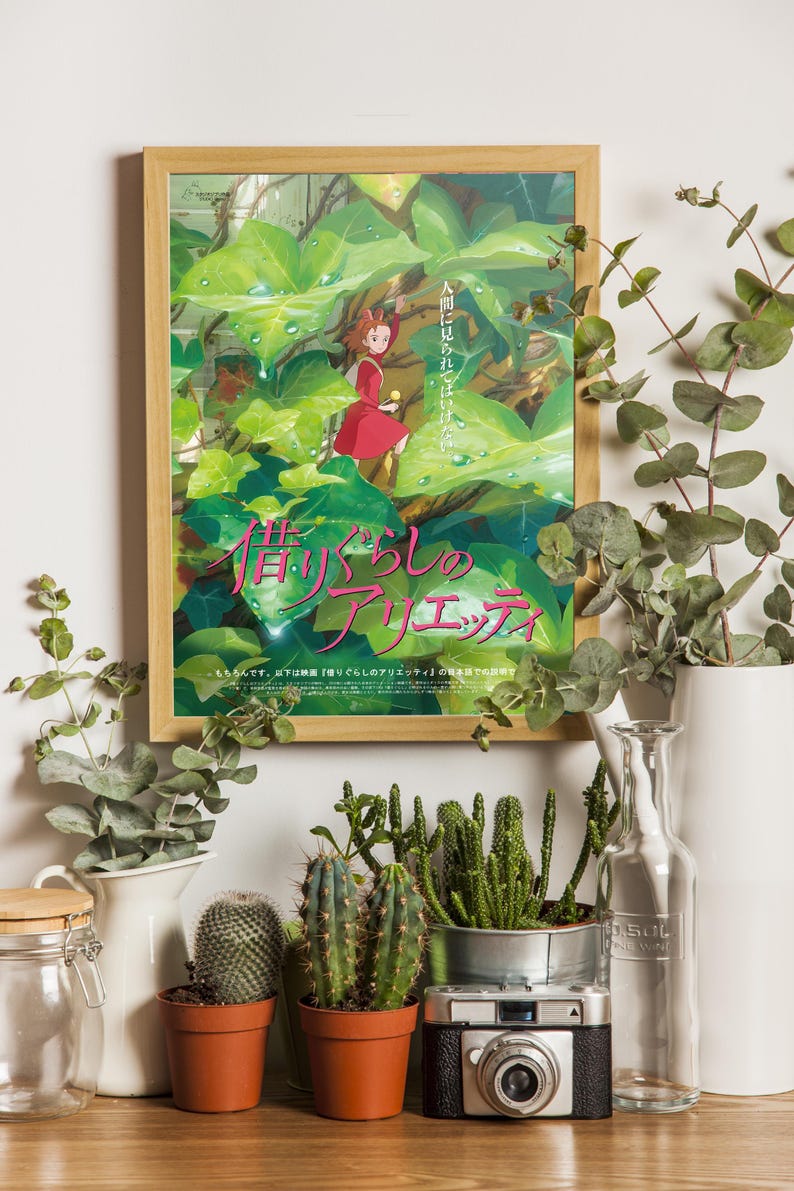 Pu&ograve; includere: Una locandina cinematografica incorniciata di Arrietty - Il mondo segreto sotto il pavimento con un personaggio in abito rosso tra grandi foglie verdi. Il poster include testo giapponese ed &egrave; esposto accanto a cactus, una fotocamera vintage e vasi.