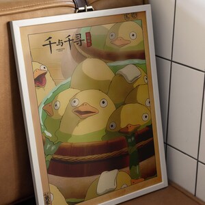 May include: A framed print of a scene from the animated film Spirited Away. The print features a group of yellow ducklings in a wooden tub, with the Japanese text "千と千尋の神隠し" (Spirited Away) at the top.