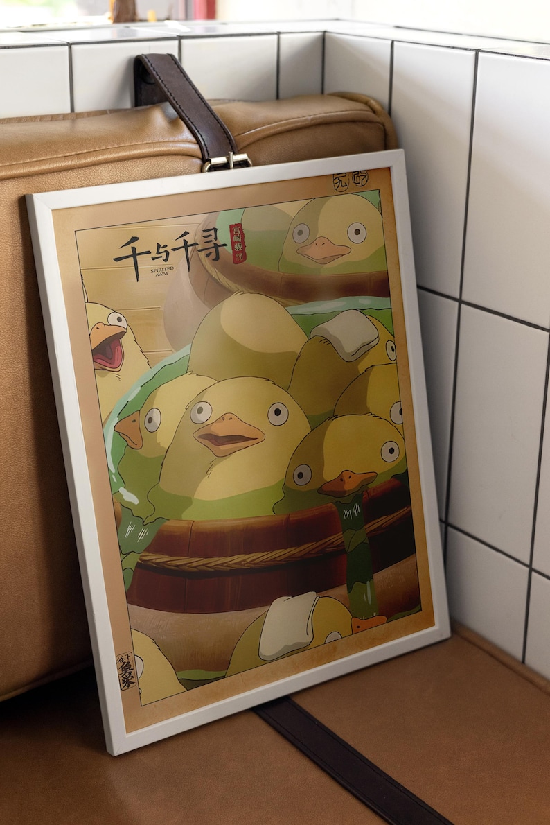 May include: A framed print of a scene from the animated film Spirited Away. The print features a group of yellow ducklings in a wooden tub, with the Japanese text "千と千尋の神隠し" (Spirited Away) at the top.